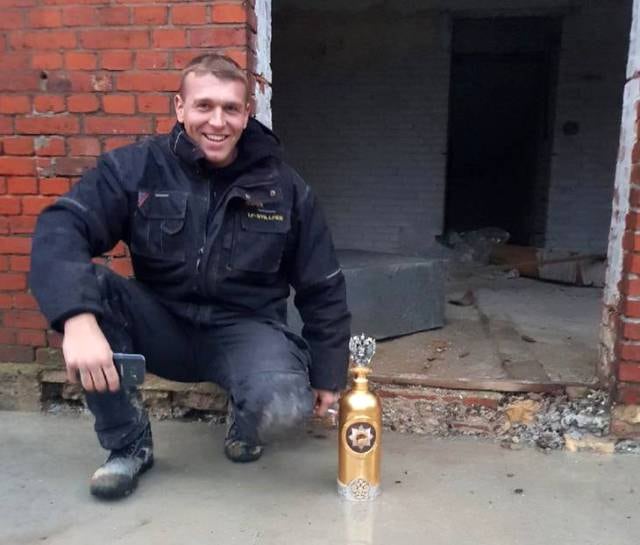 Man crouching beside a gold DARTZ RussoBaltique vodka bottle by a brick wall